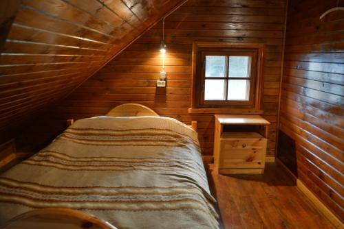ein Schlafzimmer in einem Blockhaus mit einem Bett und einem Fenster in der Unterkunft Brīvdienu māja Greiži in Dzirciems