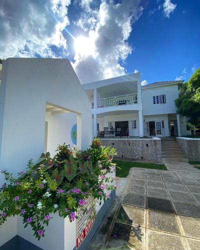 a white house with flowers in front of it at All Nations Guest House in Port Antonio
