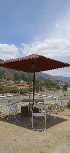 a picnic table with an umbrella and two chairs at Ecolodge Casa del Montañista in Huaraz