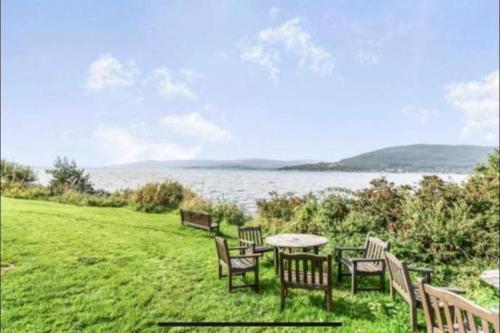 a table and chairs on a field with a view of the water at Superb Loch Side Apartment with Sea & Sunset Views in Helensburgh