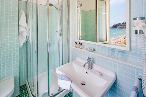 La salle de bains est pourvue de carrelage bleu, d'un lavabo et d'une douche. dans l'établissement Hotel Beau Sejour, à Alassio