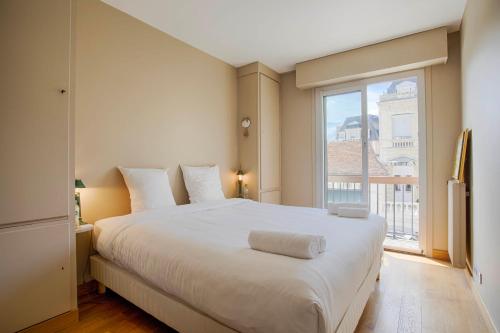 ein Schlafzimmer mit einem großen weißen Bett und einem Fenster in der Unterkunft Les Cigognes - Deux Pièces - Deauville Centre in Deauville