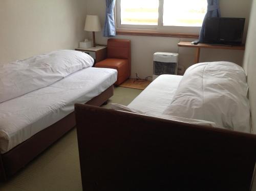 a room with two beds and a chair and a television at Pension New White Bear in Kutchan