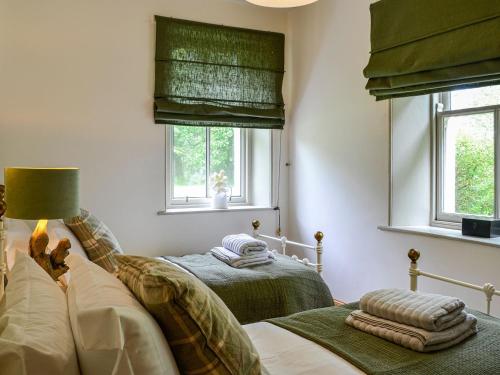 a bedroom with two beds and two windows at Milnfield Cottage in Annan