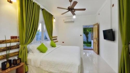 a bedroom with a bed with green curtains and a ceiling fan at Rangali Etos Guraidhoo in Guraidhoo