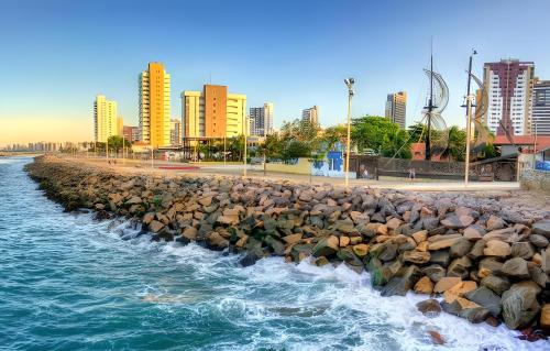 a rock wall next to the water with buildings at Top Flat Fortaleza in Fortaleza