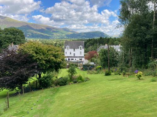 a house in a field with mountains in the background at Maple Bank Country Guest House in Keswick