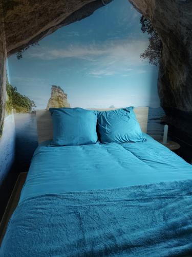 a bed with blue pillows in a cave at Le Canari in Huisnes-sur-Mer