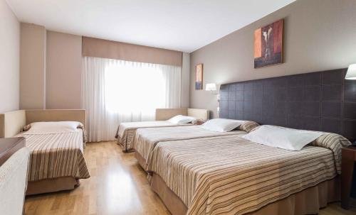 three beds in a hotel room with a window at El Patio in La Almunia de Doña Godina