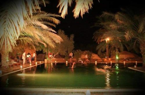 a swimming pool at night with people standing around it at Hotel Pansy in Ksar Ghilane