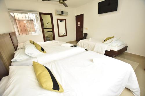a room with three beds with white sheets and yellow pillows at Hotel La Casa N. 3 in Montería
