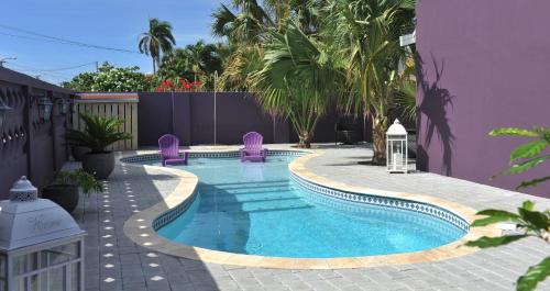 una piscina con sillas moradas junto a un edificio púrpura en Cadushi Apartments, en Oranjestad