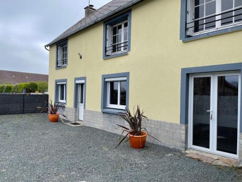 ein gelbes Haus mit drei Topfpflanzen davor in der Unterkunft Les Limicoles maison proche mer in Gouville-sur-Mer