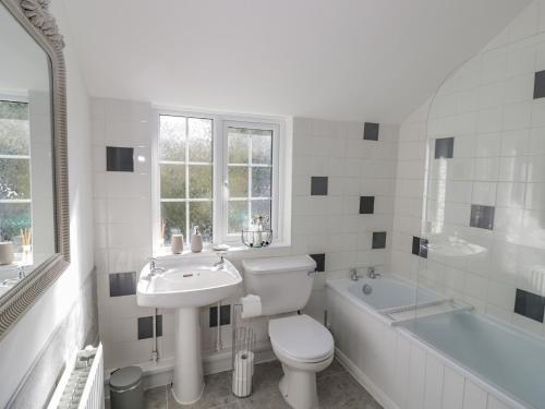 a white bathroom with a toilet and a sink and a tub at Blossom Cottage in Broadway