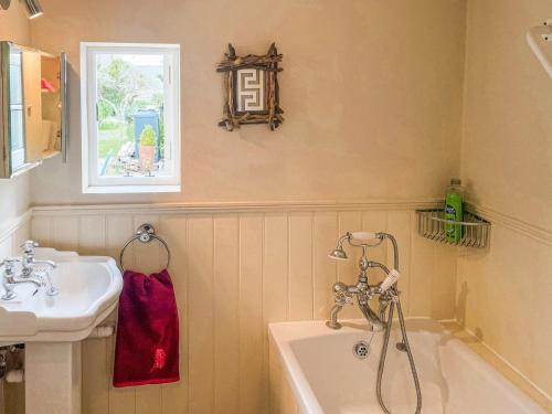 een badkamer met een wastafel, een bad en een raam bij Plum Tree Cottage in Fontmell Magna