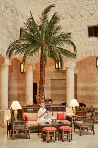 a woman sitting on a couch in a lobby with a palm tree at Mövenpick Resort Petra in Wadi Musa