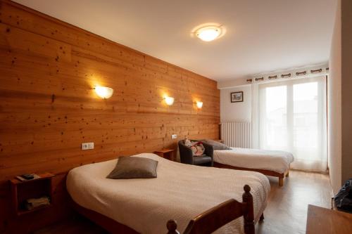 a bedroom with two beds and a wooden wall at Logis Hôtel Restaurant L'ancienne Auberge in Bolquere Pyrenees 2000