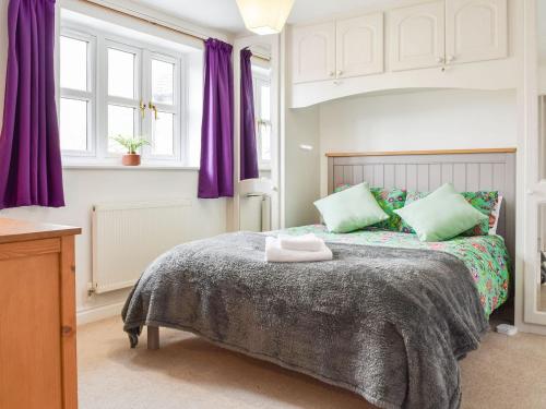 a bedroom with a large bed with purple curtains at Primrose Cottage in Little Rissington