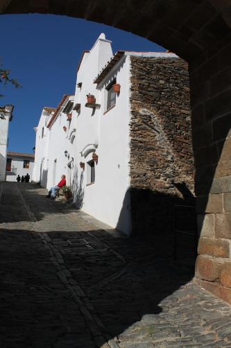 a white building with a stone wall and a person sitting on the ground at Casa Dom Dinis in Monsaraz