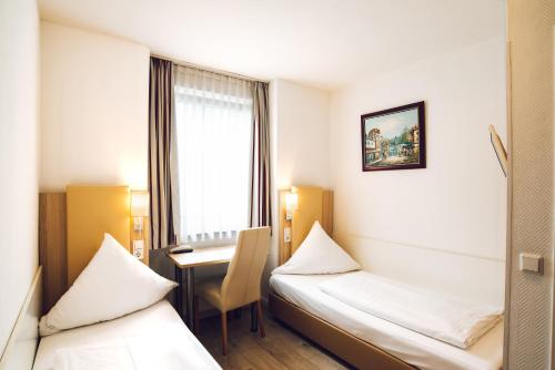 a room with two beds and a desk and a window at Hotel Domblick Garni in Cologne