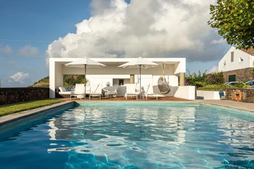 a swimming pool with chairs and umbrellas next to a house at Casa do Pico Arde in Ribeira Grande