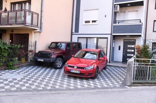dois carros estacionados num parque de estacionamento ao lado de um edifício em Demir Apartmani em Novi Pazar