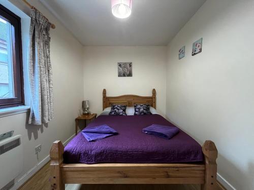 ein Schlafzimmer mit einem Bett mit violetter Bettwäsche und einem Fenster in der Unterkunft River View Apartment in Elgin
