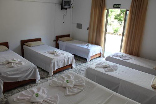 um quarto com três camas com lençóis brancos em Pousada Oliveira em Foz do Iguaçu