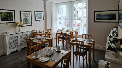 uma sala de jantar com mesas e cadeiras de madeira e janelas em Breeze B&B em Llandudno