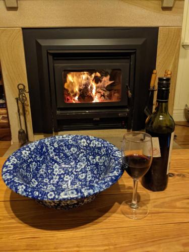 a plate and a glass of wine on a table with a fireplace at Amiens Cottage, historic, quiet, in heart of Stanthorpe in Stanthorpe