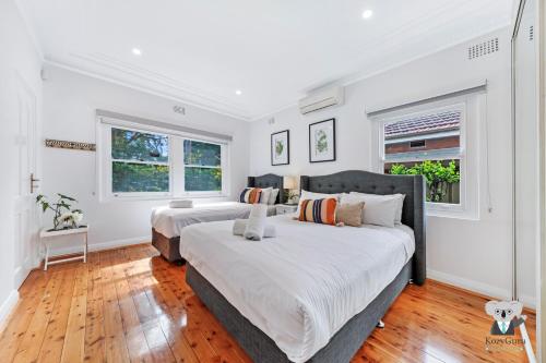 シドニーにあるKozyGuru / Rockdale / Spacious Modern 2 Bedrooms Holiday Home NRO147の白い壁とウッドフロアのベッドルーム1室(ベッド2台付)