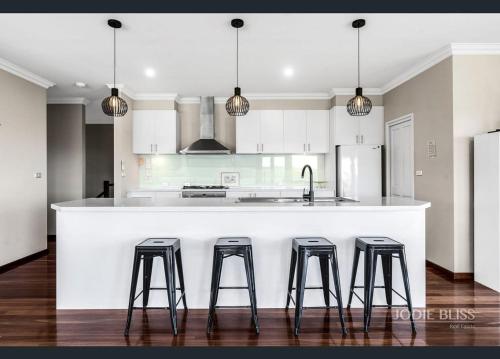 a kitchen with a white counter and four stools at Twelve Apostles Beach House B&B in Port Campbell