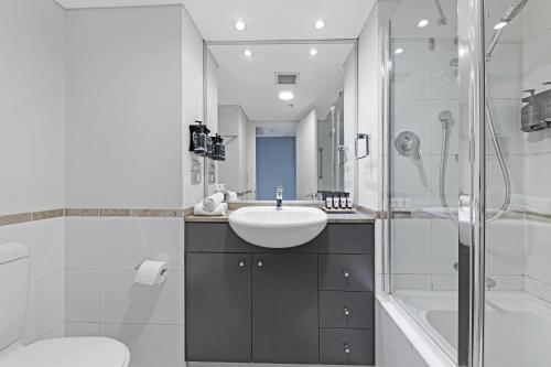 a white bathroom with a sink and a shower at KozyGuru | Sydney CBD | Freshly | 2 Bed Studio in Sydney
