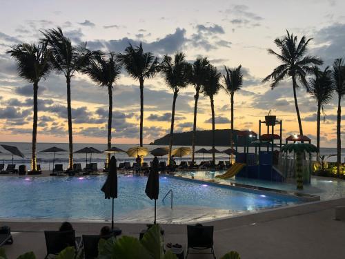 a pool with palm trees and a sunset in the background at Viaggio Resort Mazatlán in Mazatlán