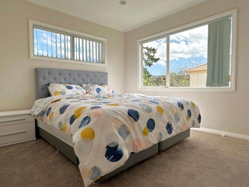 sypialnia z łóżkiem z kolorową kołdrą i dwoma oknami w obiekcie Cheerful 4 bedrooms home with stunning sunshine w Auckland
