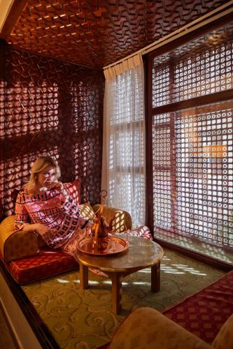 a woman sitting on a couch in a room with windows at Mövenpick Resort Petra in Wadi Musa