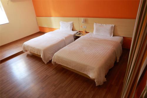 two beds in a room with orange walls and wood floors at 7Days Inn Shizheng Square in Tai'an