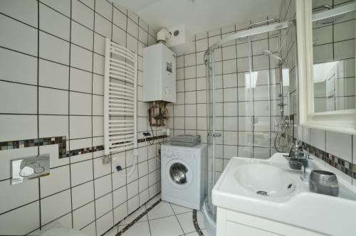 a white tiled bathroom with a washing machine and a sink at Urban Nest Apartments Bon 5 in Krakow