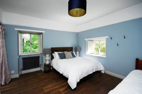 a blue bedroom with two beds and two windows at Upside Lodge - Beautiful cottage sleeps 6 near Bath Frome in Shepton Mallet