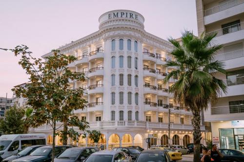 a large white building with cars parked in a parking lot at Hotel Empire Albania in Durrës