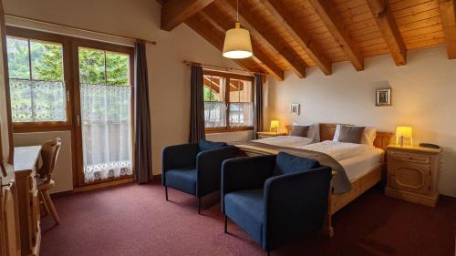 a bedroom with a bed and two blue chairs at Hotel Beau-Séjour in Leukerbad