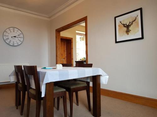 a dining room table with chairs and a clock on the wall at House by the Harbour - NC500 Route in Wick