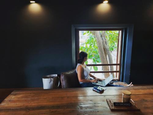 a woman sitting at a table with a laptop at The Old Quarter Hostel in Panaji
