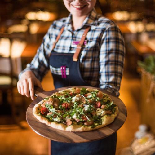 a woman holding a pizza on a wooden board at Millennium Plaza Downtown Suites in Dubai