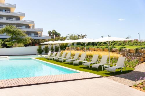 einen Pool mit Stühlen und Sonnenschirmen neben einem Gebäude in der Unterkunft Shantivillas Portimão in Portimão