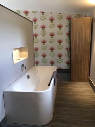 a white tub in a bathroom with flowers on the wall at Garden Room Lodges in Alexandria