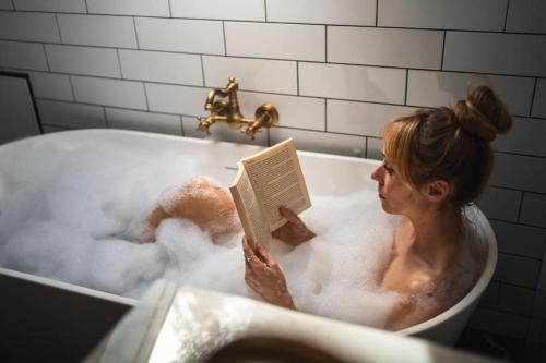 グラスゴーにあるThe West End Loft - 5* Retreat - Private Parking!の浴槽に腰掛けて本を読む女性