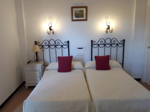 Duas camas num quarto com duas almofadas vermelhas em Hostal 2 estrellas -Restaurante Las Tres Encinas em Cabeza la Vaca
