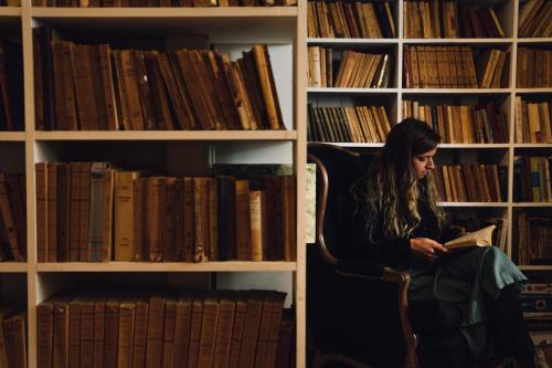 une femme assise sur une chaise en lisant un livre dans une bibliothèque dans l'établissement Auberge sur Mer, à Notre-Dame-du-Portage