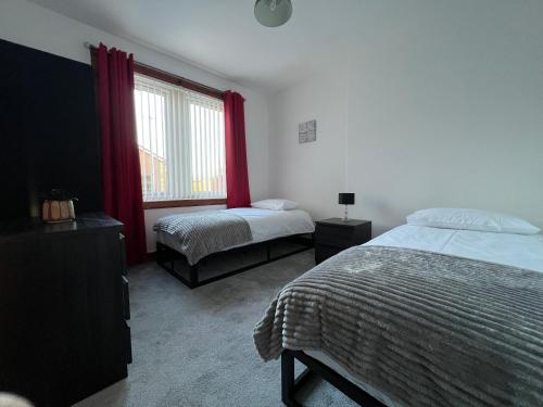 a bedroom with two beds and a window with red curtains at Lomond View Apartment in Ladybank